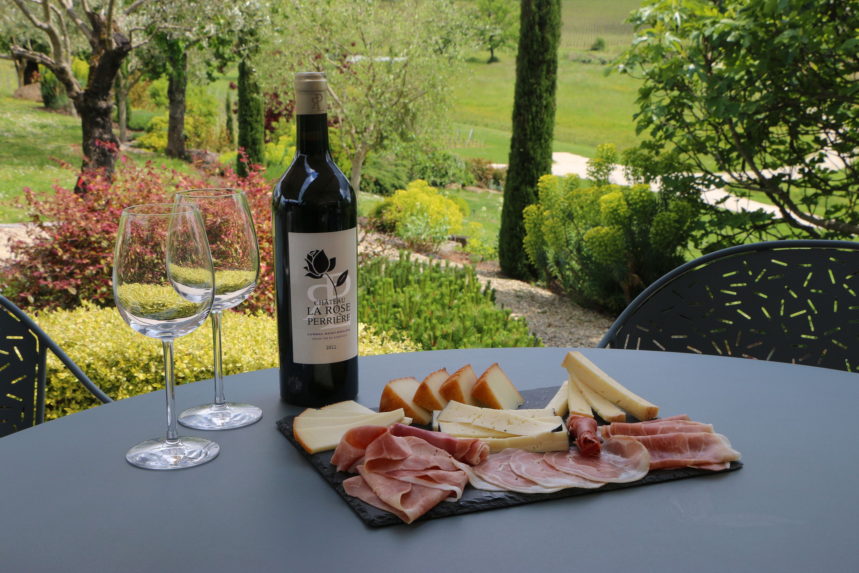 une suggestion d’accord avec un vin rouge Château La Rose Perrière : une planche de fromages et de charcuterie posée sur une table sur la terrasse du château.