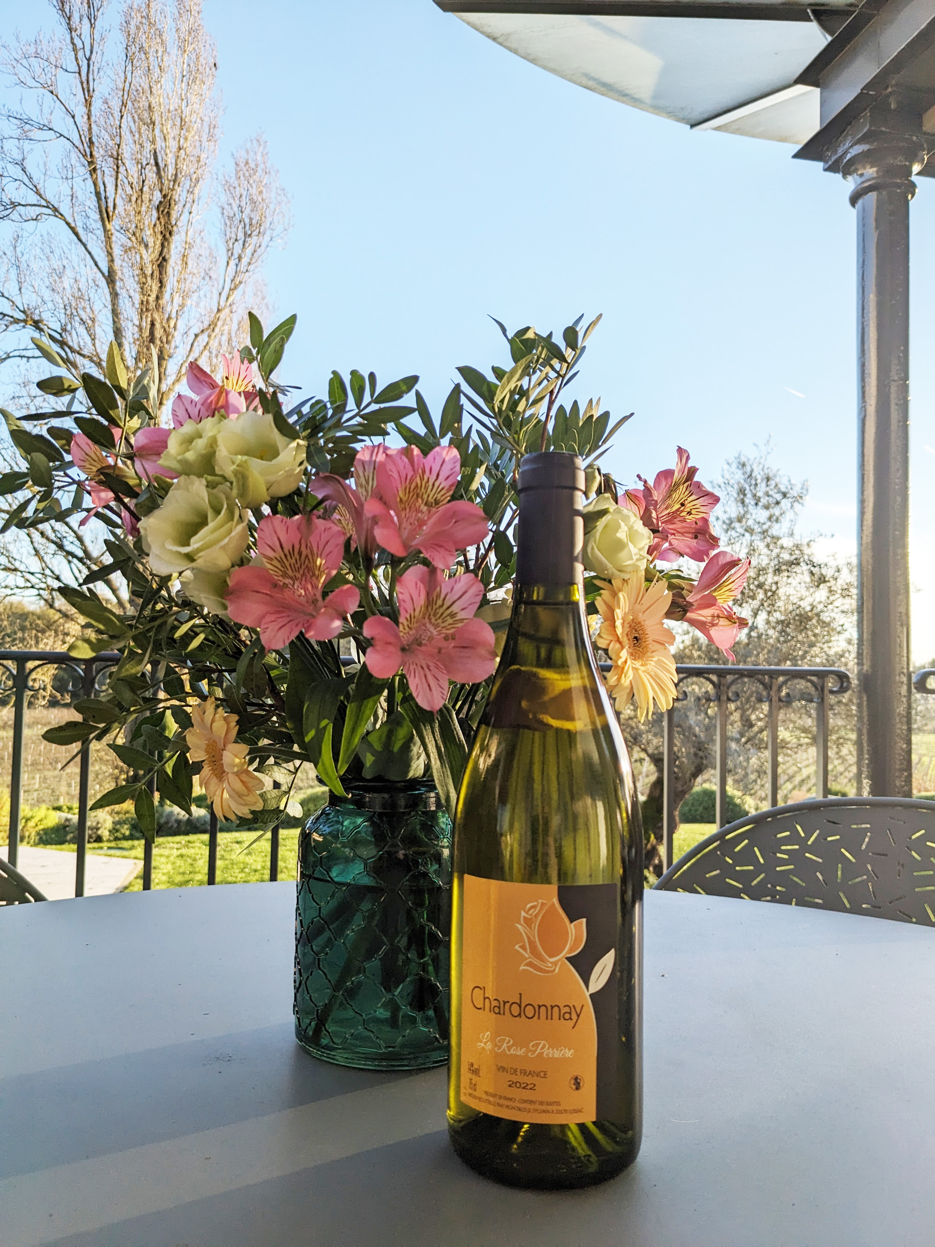 Bouteille de Chardonnay La Rose Perrière sur une table de la terrasse à côté d’un bouquet de fleurs naturelles