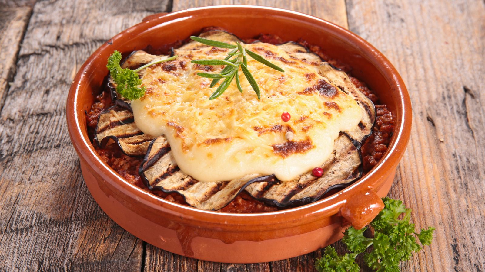 Moussaka dans un plat rond de terre cuite posé sur une table en bois