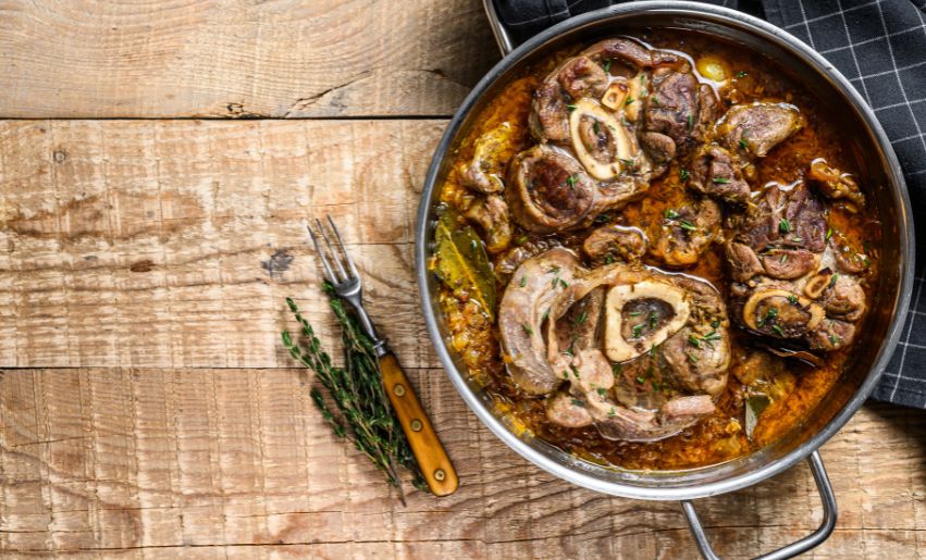 ALT Plat d Osso B uco posé sur une table en bois à côté d une serviette grise à c arreaus et d une fourchette metallique